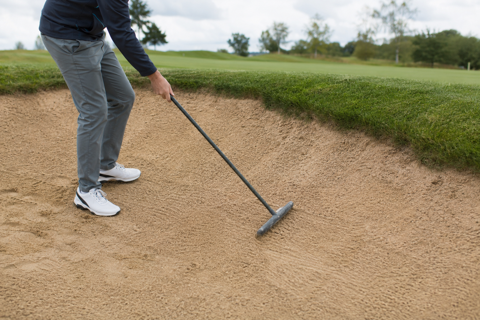 Golfer smoothing footprints and club marks with a bunker rake